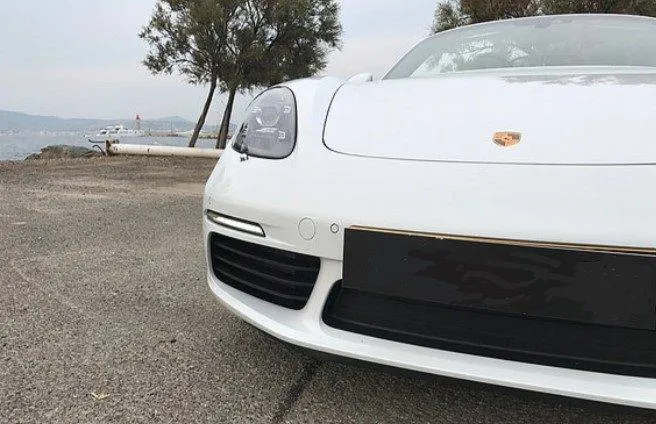 White sports car parked on scenic paved area near trees and water.