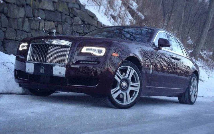 Luxurious burgundy Rolls-Royce in snowy mountain setting.